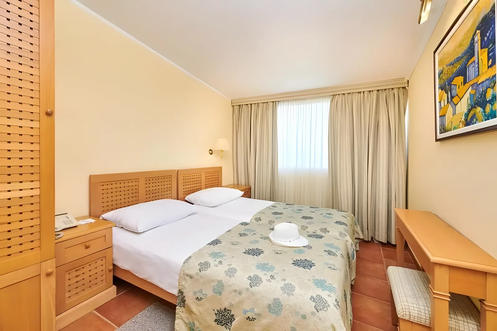 Soba sa dva kreveta, drvenim uzglavljem i prekrivačem sa šarom pored prozora · Istra - Poreč - Leto 2026. - Apartmani Bellevue Plava Laguna 4*