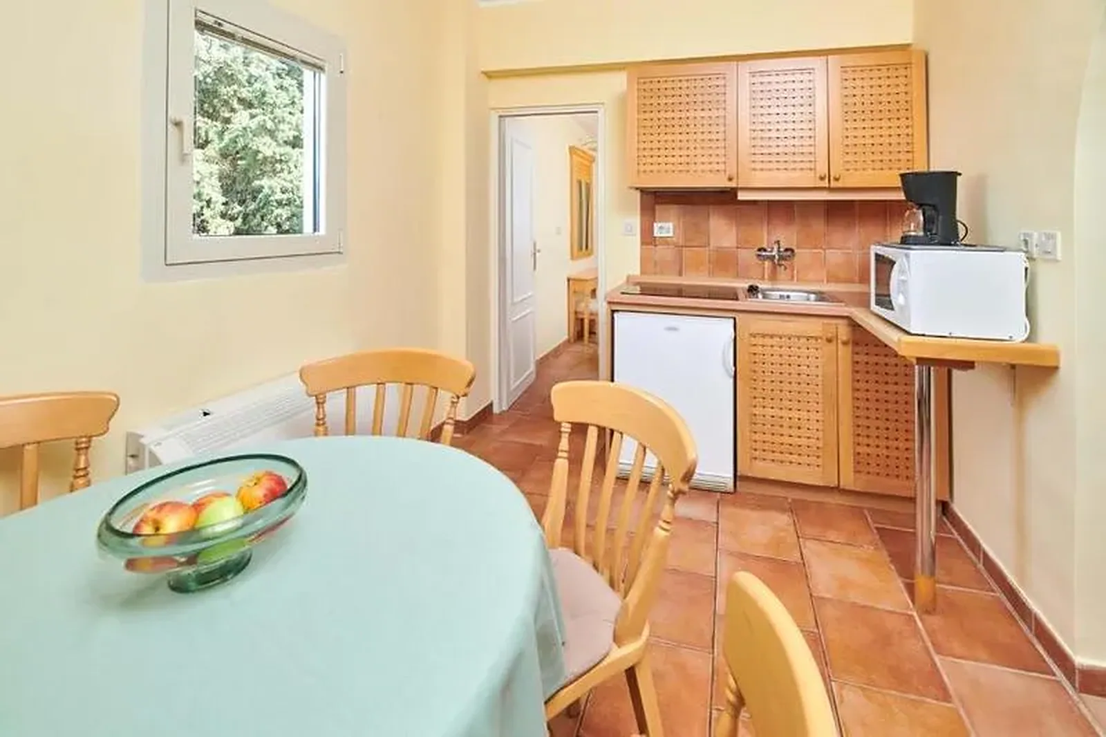 Kuhinja sa drvenim elementima, trpezarijskim stolom i pogledom na vrt kroz prozor · Istra - Poreč - Leto 2026. - Apartmani Bellevue Plava Laguna 4*