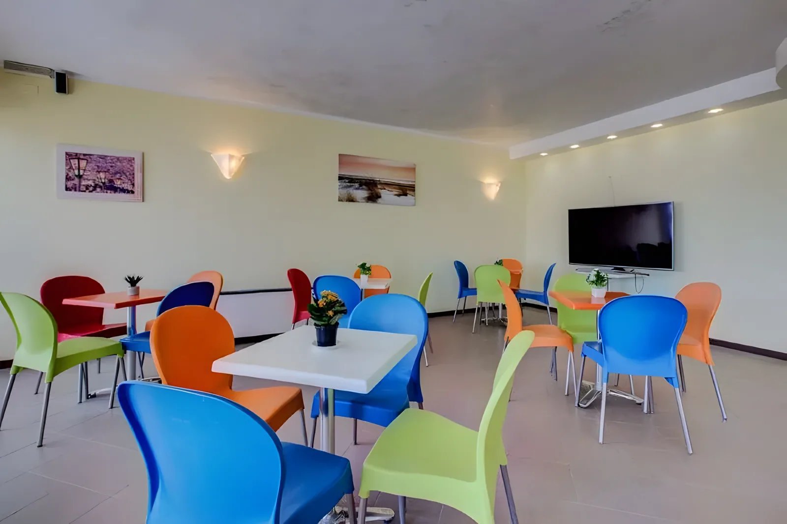 Šareni zajednički prostor sa trpezarijskim stolovima i televizorom · Hotel Barone, Viserbella