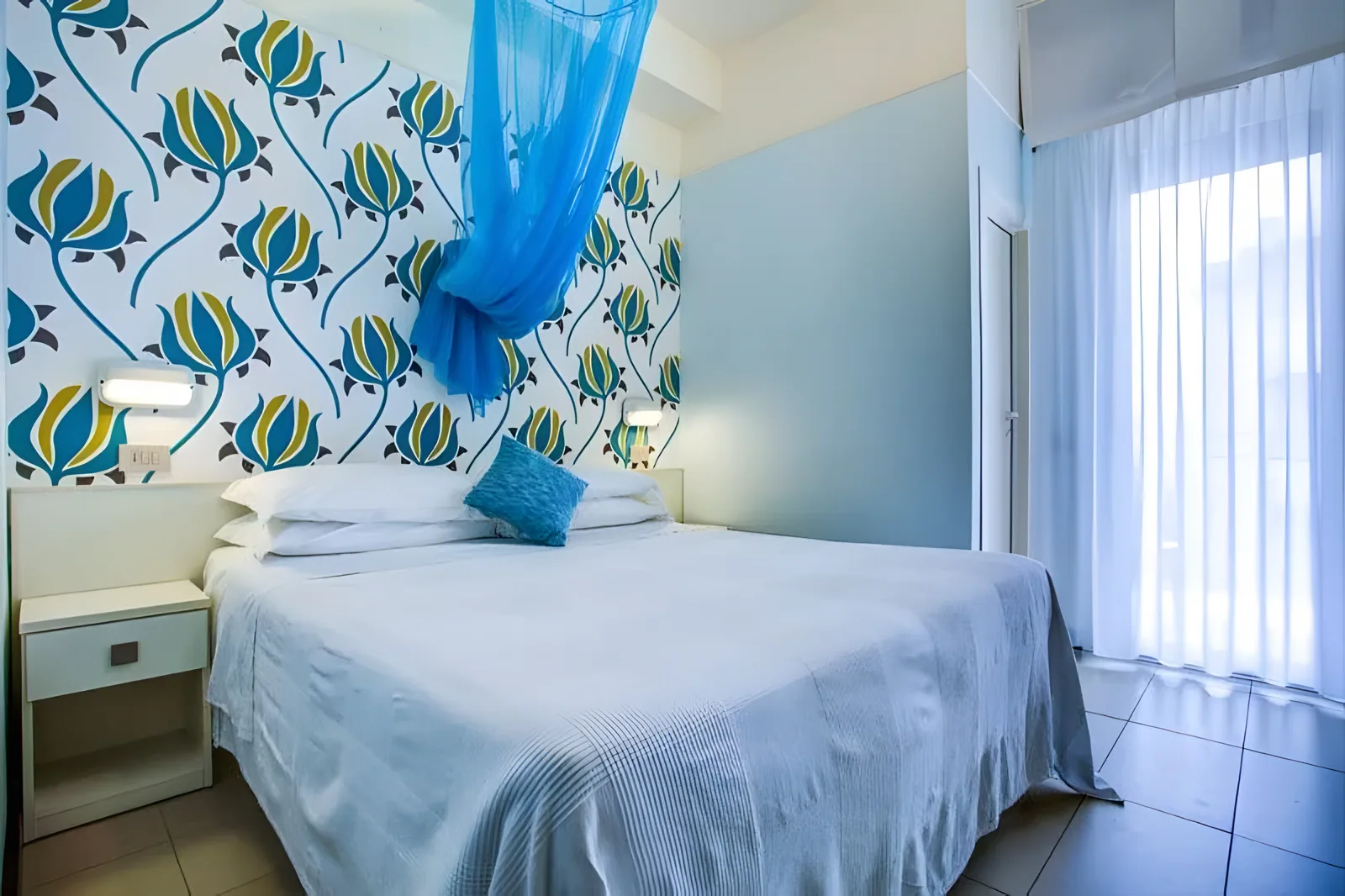 Spavaća soba sa šarenim uzglavljem i plavim prozirnim baldahinom · Hotel Konrad, Marebello